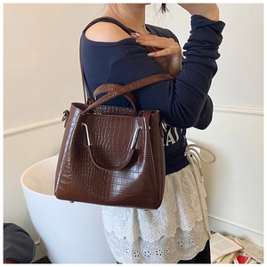 Detail of dark brown crocodile-textured bucket bag with dual handles and metal rivets