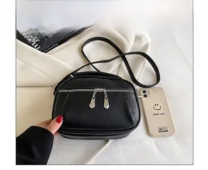 Close-up of black pebble leather crossbody bag with dual zippers showing size comparison