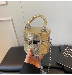 Detail of gold cylindrical evening bag with quilted glitter texture and metal chain