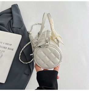Detail of white quilted cylinder bag with silver chain strap and lace bow accent