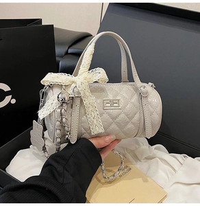 Detail of cream quilted cylinder bag with silver twist lock and lace bow charm