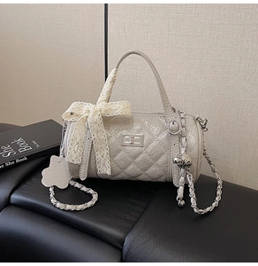 Close-up of beige quilted barrel bag featuring a metal twist lock and lace bow detail