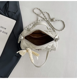 Detail of cream quilted cylindrical bag with chain strap and lace bow charm