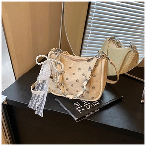 Detail of beige quilted handbag featuring silver studs, pearl bow and lace tassel charms