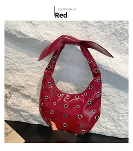 Detail of red patent leather hobo bag featuring silver eyelets and a knotted handle design