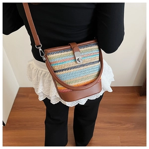 Detail of woven straw bucket bag with colorful stripes and brown leather strap on model