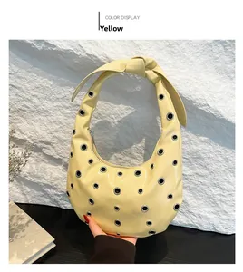 Detail of yellow crescent shoulder bag with metallic eyelets and knotted strap design