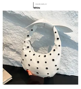 Detail of white half-moon shoulder bag with eyelet studs and knotted bow handle