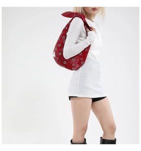 Chic red patent leather hobo bag with silver eyelets and knot detail on a model