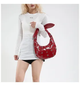 Detail of red patent leather shoulder bag with metal eyelets and a bunny ear knot