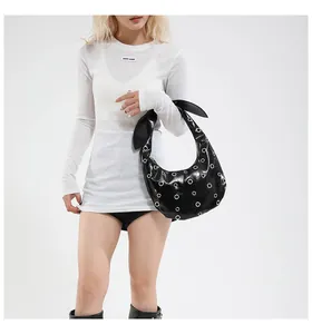 Detail of black patent leather crescent bag with silver eyelets and knotted bow handle