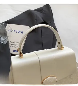 Detail of white textured leather handbag with gold hardware and curved handle