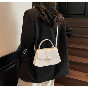 Detail of white leather handbag with snakeskin texture and golden M buckle on black suit