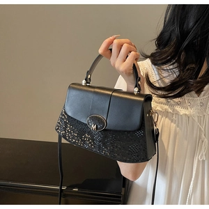 Detail of black handbag showing matte leather stitching and snake pattern embossing