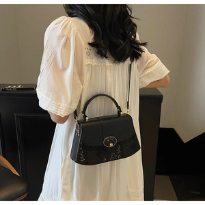 Model wearing a black matte leather bag with snake pattern detail and gold M buckle hardware