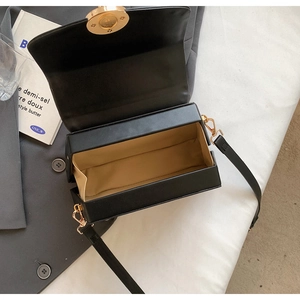 Detail view of the black structured box bag showing its beige lining and gold twist lock