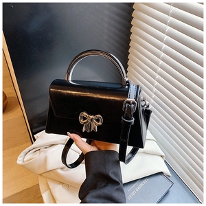 Detail of glossy black leather handbag with silver metal bow and curved handle