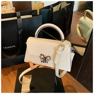 Close-up of a cream crossbody bag featuring a silver metal bow buckle and smooth leather texture