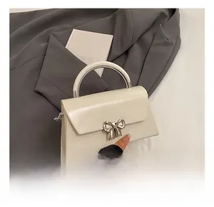 Detail of white trapezoid handbag with silver metal bow buckle on a minimalist desk