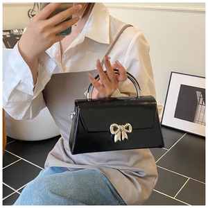 Detail of black patent leather handbag with silver bow metal buckle and curved metal handle