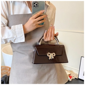 Detailed close-up of dark chocolate glossy crossbody bag with silver bow accent