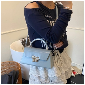 Detail of light blue crossbody bag with silver bow clasp worn by model at side