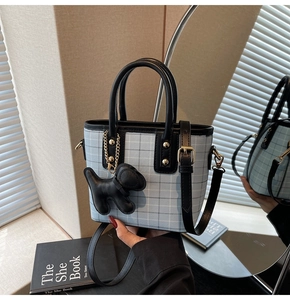 Close-up of light blue plaid handbag with black leather trim and cute puppy charm