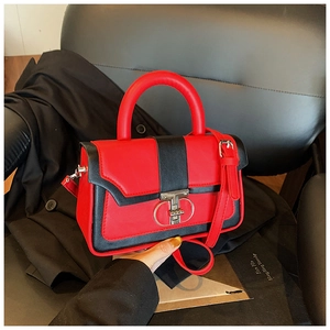 Detail of red and black crossbody bag with metallic lock on leather background