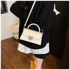 Detail of off-white crossbody bag featuring a silver bow buckle and semi-circular handle