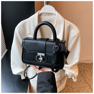 Detail of a black leather handbag with a silver twist lock and round handle against a blazer