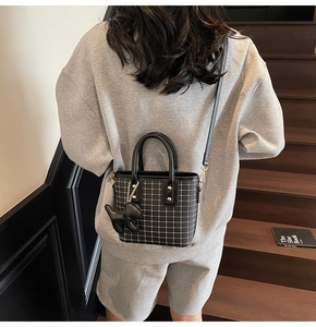 Detail of black checkered crossbody bag with dog charm on wooden stairs