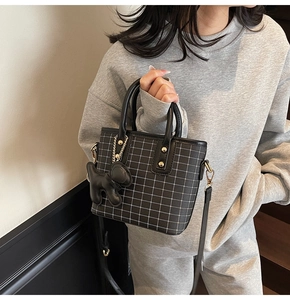 Detail of black plaid tote bag featuring a cute puppy charm and adjustable strap