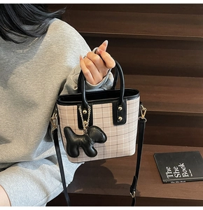 Detail of retro plaid tote bag with black leather handles and dog charm on wooden steps