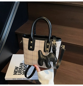 Detail of checkered tote bag with leather trim and cute puppy charm on wooden steps