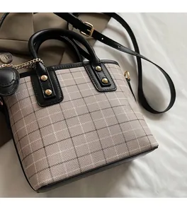 Detail of plaid canvas bag with black leather trim, golden studs, and chain strap