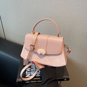 Pink crossbody handbag with snakeskin texture and gold M-logo clasp on a book base
