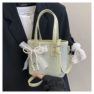 Close-up of light green straw bag with pearl lace bow and heart metal pendant