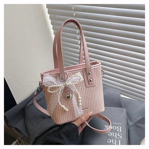 Pink woven straw handbag featuring delicate lace and pearl bow charms held by a model