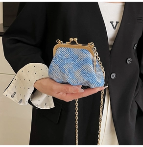 Close-up of blue textured fabric chain bag with gold metal clasp on model attire