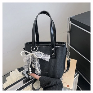 Detail of woven black tote bag with pearl bow, lace trim, and heart pendant