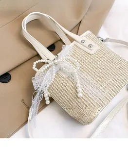Detail of beige straw handbag with pearl bow, lace ribbons and white leather strap