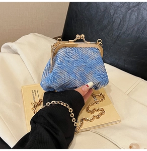 Detail of blue woven kiss-lock bag with gold frame and chunky chain strap on a book