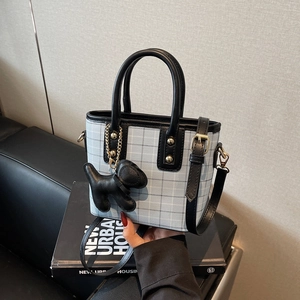 Blue and grey plaid handbag with black leather trim and dog charm on a sofa