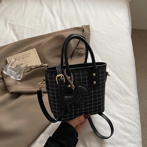 Classic black plaid handbag with gold hardware and a cute dog charm on a white background