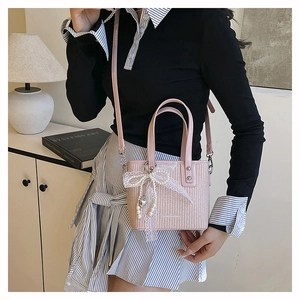 Detailed close-up of pink woven mini tote bag with white lace bow and pearl charm