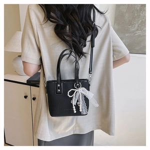 Detailed view of black textured handbag with pearl bow charm worn on shoulder