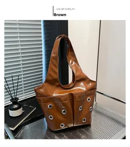 Close-up of brown glossy tote bag featuring silver metal eyelets and industrial pockets