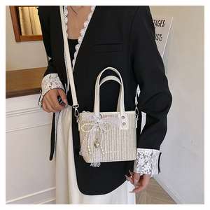 Detail of hand-woven straw bag featuring a large lace bow and pearl chain on a model