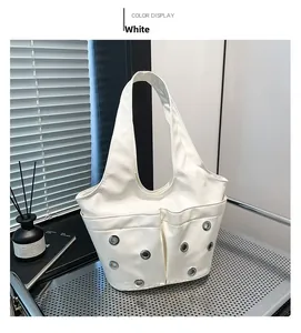Detailed view of a white leather underarm bag with grommet accents on metal table
