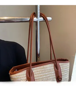Detailed close-up of woven straw tote bag featuring brown leather trim and slim shoulder straps